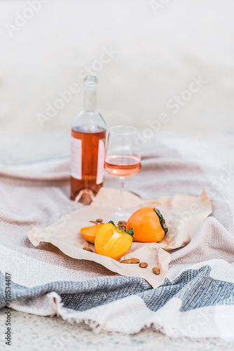 Picnic on the beach with persimmons, almond and bottle of rose wine on beige blanket. photo