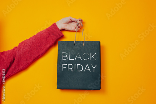 Woman holds black bag. Black friday image on the orange background. Hand and black friday bag.