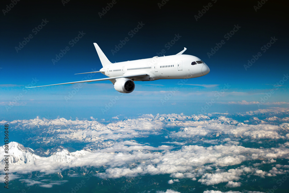 White passenger plane in flight. The plane flies above a snow covered mountain landscape. Aircraft front view. White passenger plane in flight. The plane flies above a snow covered mountain landscape. Aircraft front view.