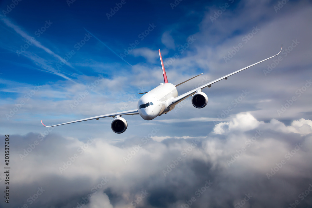 White passenger plane in flight. The plane flies against a background of a cloudy sky. Aircraft left inclination / front view.