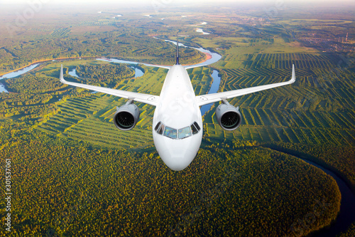 White passenger plane in flight. The plane flies against a background of a forest and river. Aircraft front view.