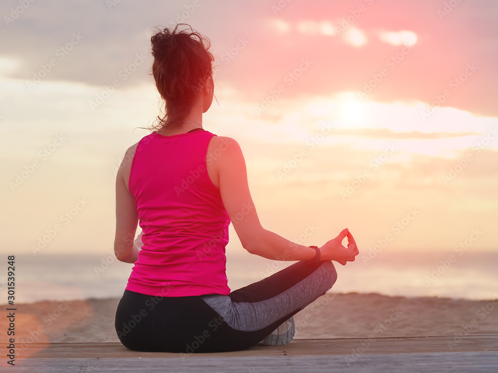 Beautiful woman practicing yoga on a wooden pier. Sea and sunset sky background.