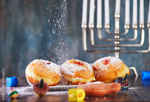 Jewish holiday Hanukkah background. A traditional dish is sweet donuts. Candlestick with candles and spinning tops on a blue background. Sprinkle donuts with powdered sugar. Copy space. photo