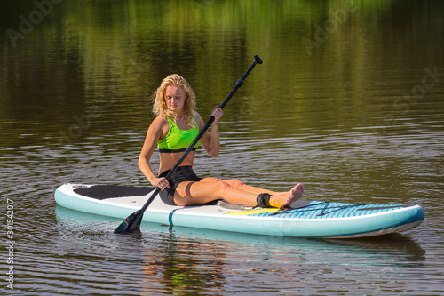 Sitting young woman paddling with SUP on water