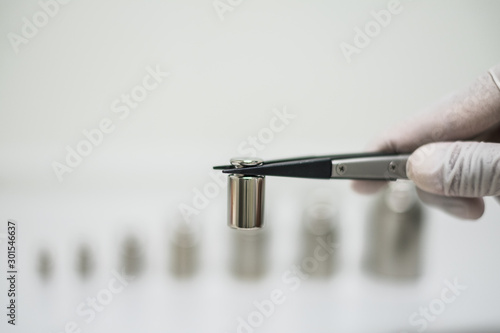 stainless steel calibration weights handle by rubber forceps with light gray background