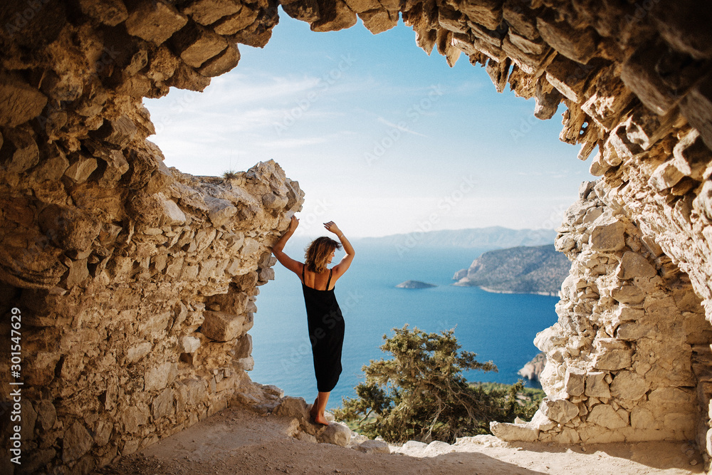 View from Monolithos, landscape at the island Rhodes, Greece. Girl admires the beauty of the landscape - obrazy, fototapety, plakaty 