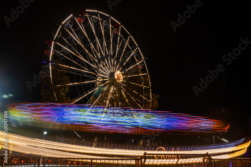 Two rides in motion in amusement park, night illumination. Long exposure. photo