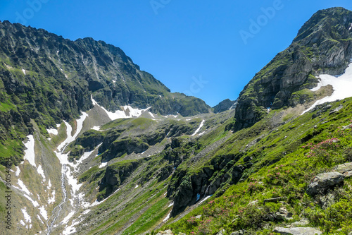 A panoramic view on Schladming Alps, partially still covered with snow. Spring slowly reaching the tallest parts of the mountains. Sharp peaks, slopes partially overgrown with lush green plants.