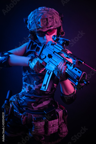the girl in military overalls airsoft posing with a gun in his hands on a dark background in the haze in neon light © rotozey