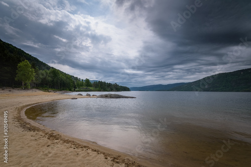 View over Byglandsfjorden lake from beach with dark clouds Norway