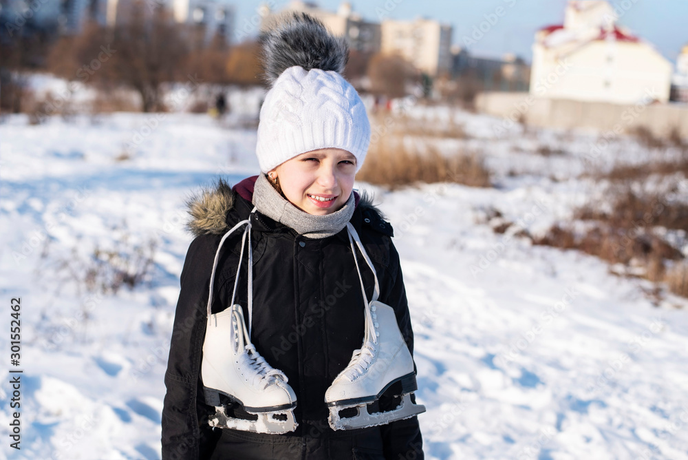 A beautiful young girl in winter warm clothes turning back from the sports school to home where she skated. White ice skates hang from her neck A beautiful young girl in winter warm clothes turning back from the sports school to home where she skated. White ice skates hang from her neck