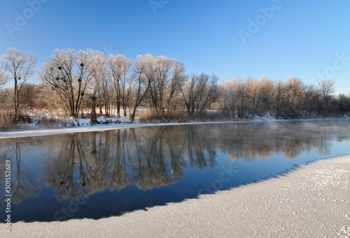 Partially melted lake on a background of snowy trees and blue sky on a sunny warm spring day. The concept of the new season and the thaw. Beauty of nature concept
