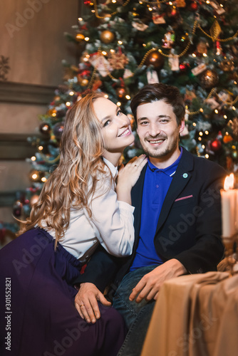 couple of beautiful young blonde girl her boyfriend on background merry Christmas happy new year tree lights with star gift decor. Family shooting