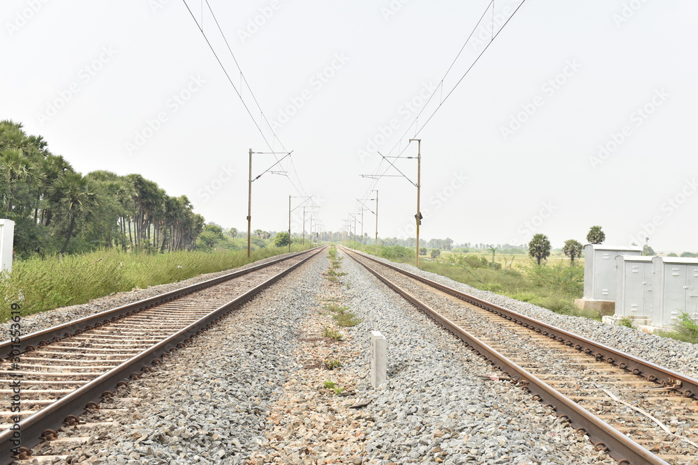railway track with the background of sky, and green trees on both sides of the track.