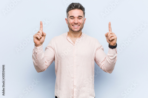 Young handsome cool man indicates with both fore fingers up showing a blank space.
