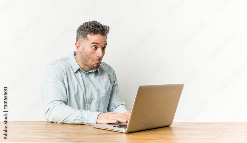 Young handsome man working with his laptop shrugs shoulders and open eyes confused. Young handsome man working with his laptop shrugs shoulders and open eyes confused.