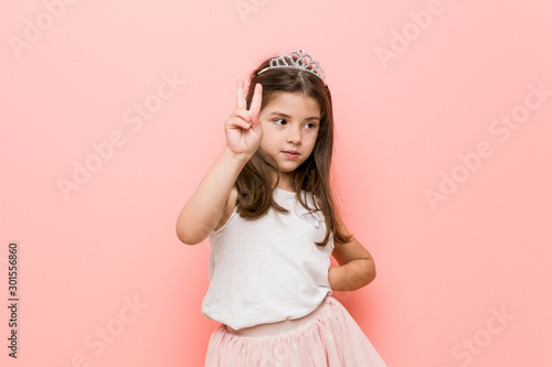 Little girl wearing a princess look joyful and carefree showing a peace symbol with fingers.