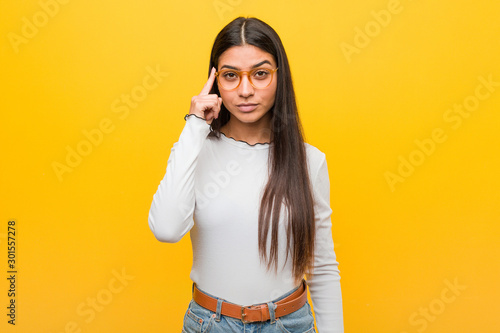 Canvas-taulu Young pretty arab woman against a yellow background pointing temple with finger, thinking, focused on a task