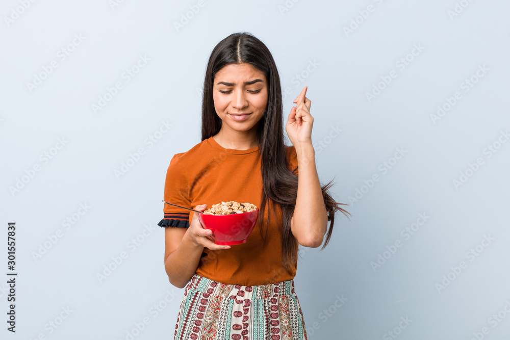 Young arab woman holding a cereal bowl crossing fingers for having luck Young arab woman holding a cereal bowl crossing fingers for having luck