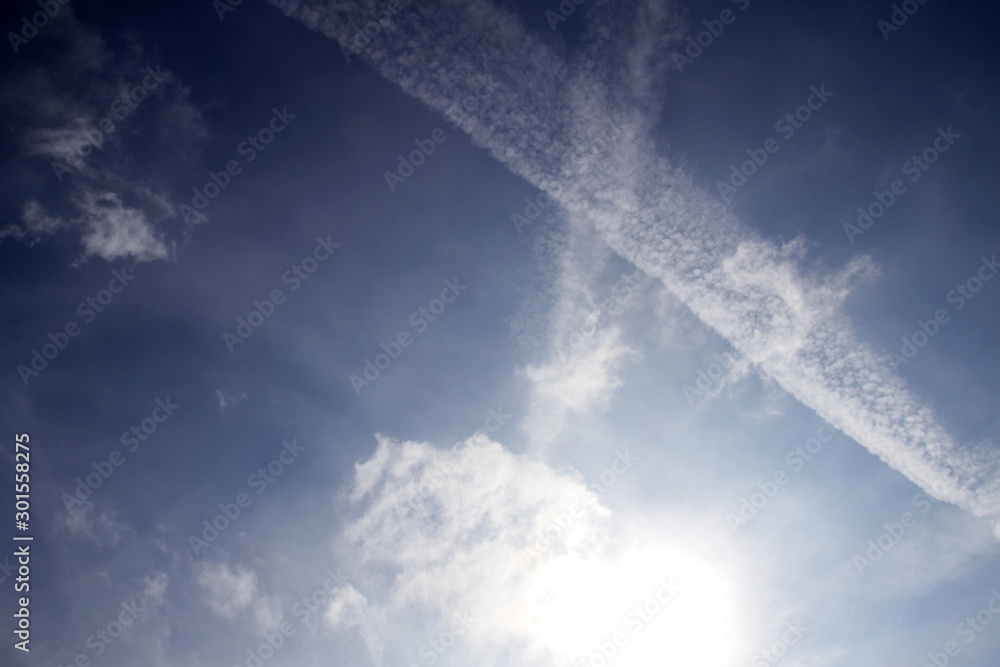 Multiple aiplane trails, chemtrails or jet trails over blue sky background. Clouds and sun Multiple aiplane trails, chemtrails or jet trails over blue sky background. Clouds and sun