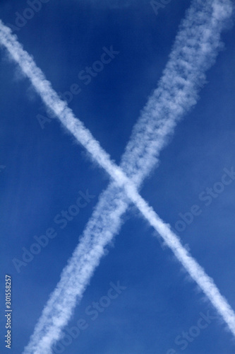 Multiple aiplane trails, chemtrails or jet trails over blue sky background. cross check