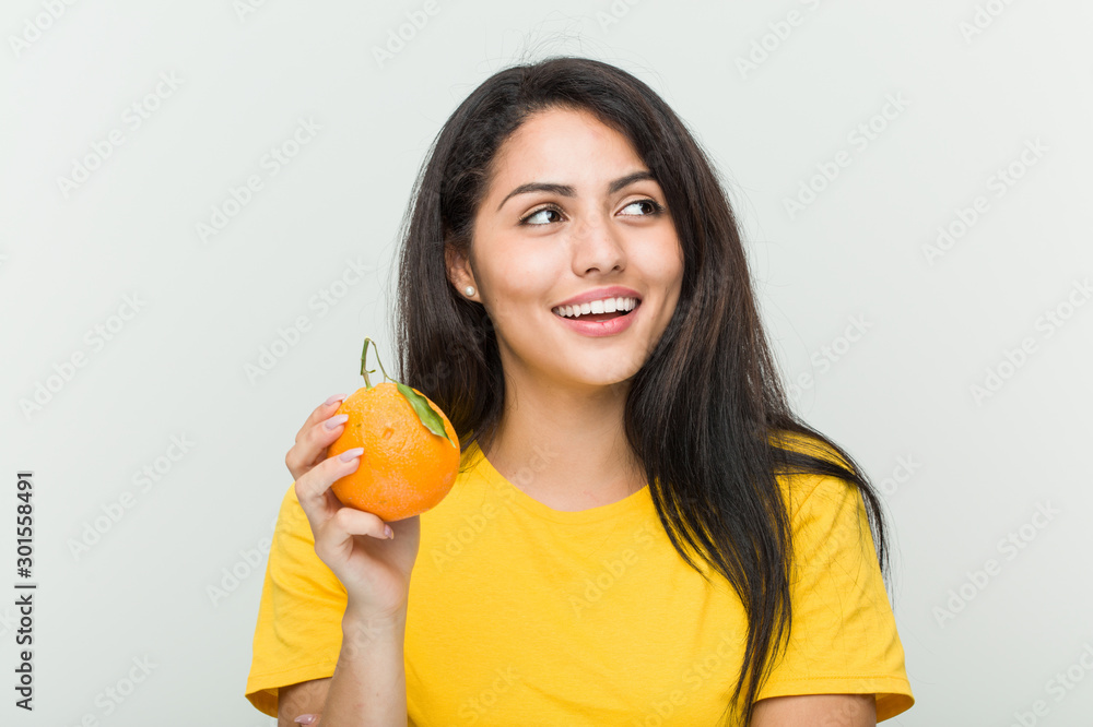 Young hispanic woman holding an orange smiling confident with crossed arms. Young hispanic woman holding an orange smiling confident with crossed arms.