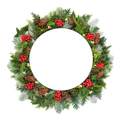 Christmas & New Year table setting with round porcelain plate with natural winter holly, snow covered fir, mistletoe, ivy, cedar leaves & pine cones on white background. Festive theme.