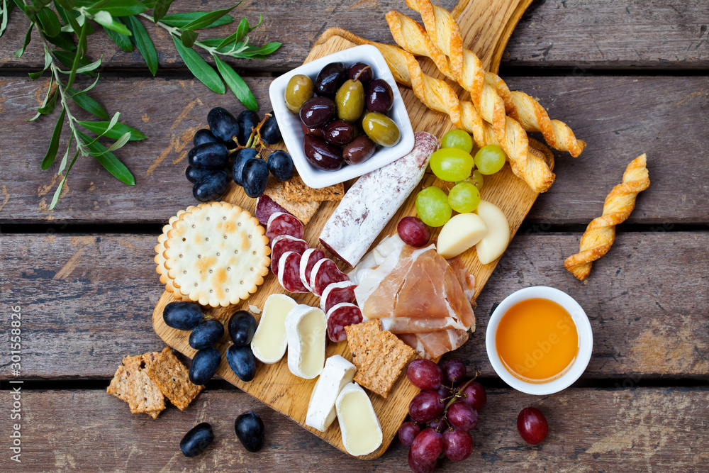 Fototapeta premium Cheese and meat appetizers on cutting board on wooden background. Top view.