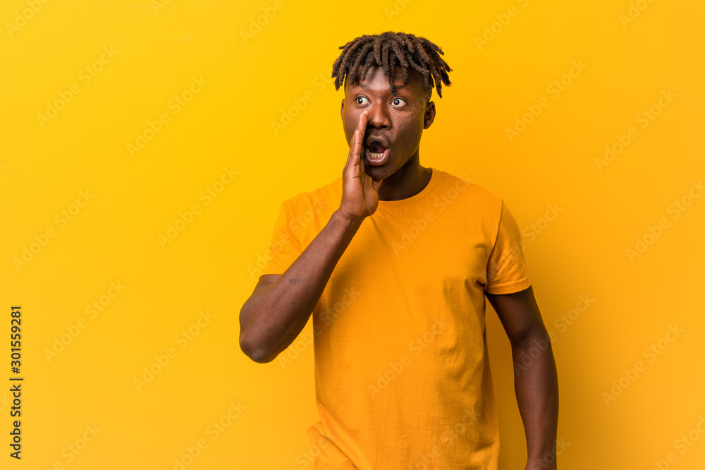 Fototapeta premium Young black man wearing rastas over yellow background is saying a secret hot braking news and looking aside