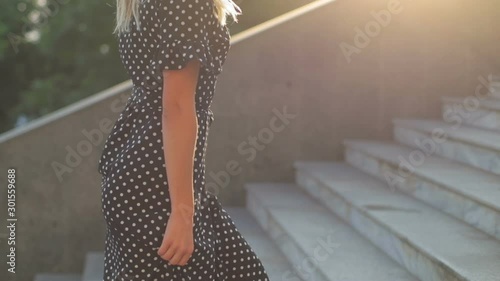 young woman in high heels goes up long stairs and fixes loose hair talking on modern smartphone low angle shot