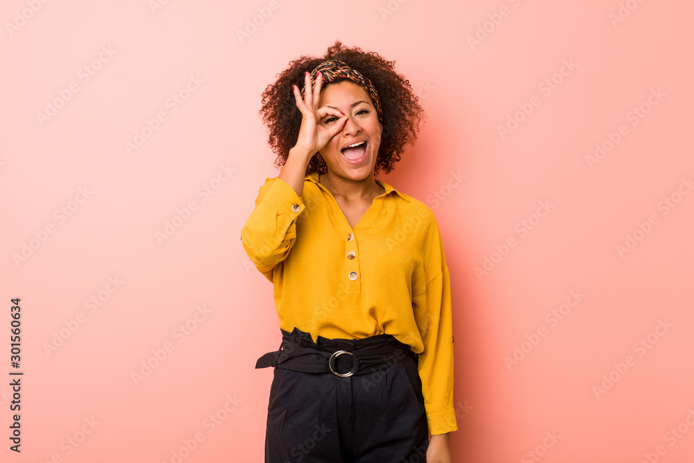 Young african american woman against a pink background excited keeping ok gesture on eye. Young african american woman against a pink background excited keeping ok gesture on eye.