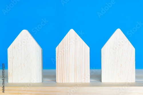 Three wooden houses on a blue background. Models of residential buildings stand on a wooden surface.