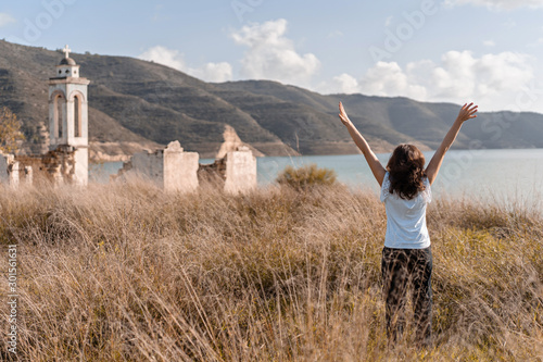 Beautiful tourist girl look on the Scenic landscape of Kouris reservoir large artificial lake and Ruined church of Ayios Nikolas staying on dam during a sunny day, Limassol district, Cyprus photo