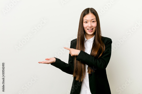 Young pretty chinese business woman excited holding a copy space on palm.