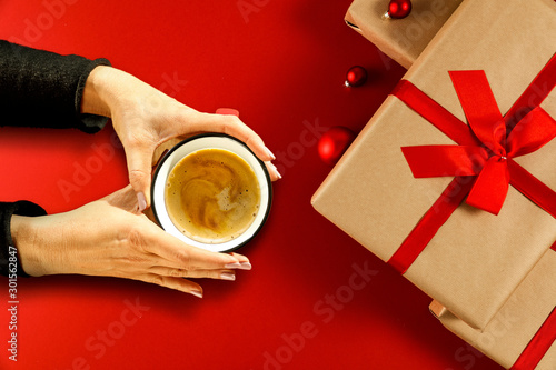 Christmas composition of ecological gifts with red ribbon and bow.Female hands wrapped gifts.Cup of coffee in women's hands and time of Christmas rest.Top view,flat lay,copy space,aerial xmas photo.