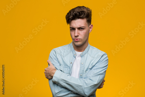 Young handsome student wearing a denim shirt frowning face in displeasure, keeps arms folded.