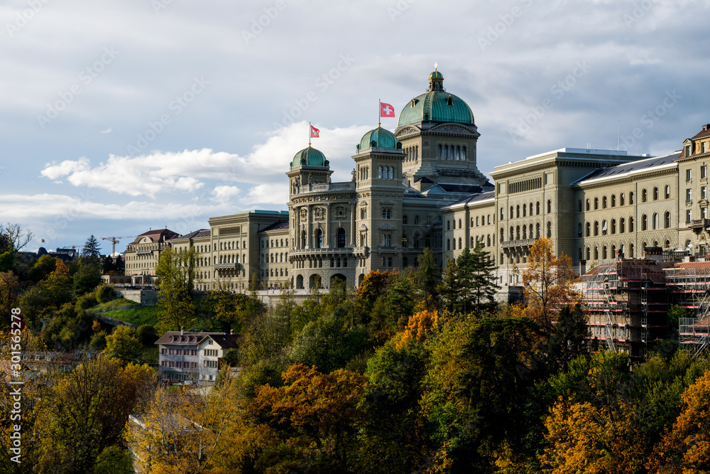 The Swiss Parliament Building (1902) with river Aare called Bundeshaus in Berne with waving swiss flags.