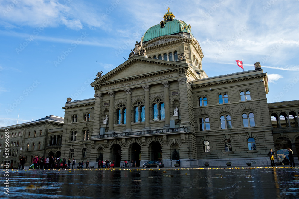 The Swiss Parliament Building (1902) with river Aare called Bundeshaus in Berne with waving swiss flags.
