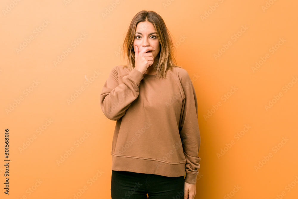 Young authentic charismatic real people woman against a wall thoughtful looking to a copy space covering mouth with hand. Young authentic charismatic real people woman against a wall thoughtful looking to a copy space covering mouth with hand.