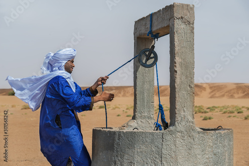 Moroccan man dressed in a traditional gandora at a well in the Sahara desert.
