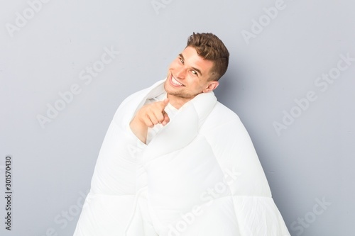 Young man holding a nordic duvet cheerful smiles pointing to front.