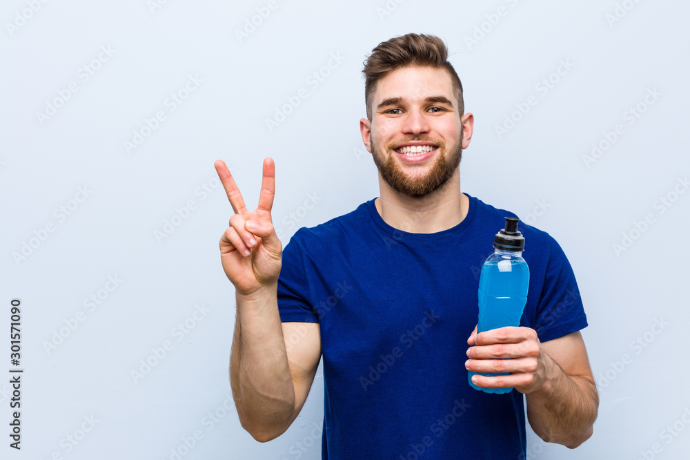 Young caucasian sportsman holding an isotonic drink showing number two with fingers. Young caucasian sportsman holding an isotonic drink showing number two with fingers.