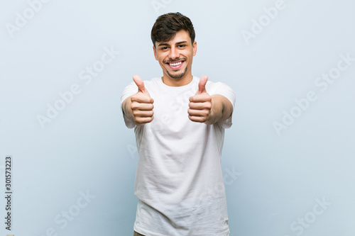 Young caucasian man wearing a white tshirt with thumbs ups, cheers about something, support and respect concept. photo