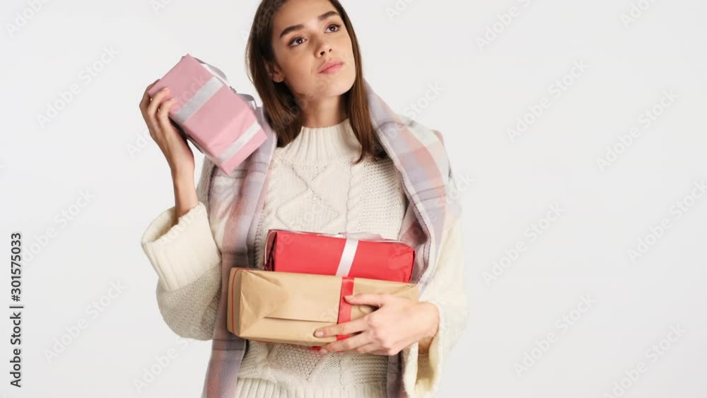 Beautiful girl with cozy plaid on shoulders shaking gift box and happily trying guess what is there over white background Beautiful girl with cozy plaid on shoulders shaking gift box and happily trying guess what is there over white background