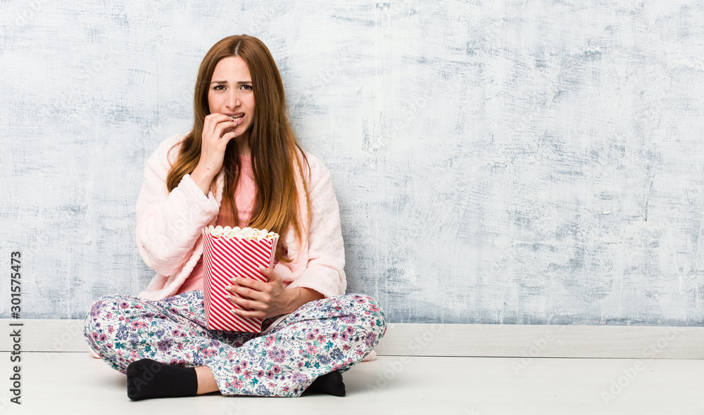 Young caucasian woman holding a popcorn bucket biting fingernails, nervous and very anxious. Young caucasian woman holding a popcorn bucket biting fingernails, nervous and very anxious.