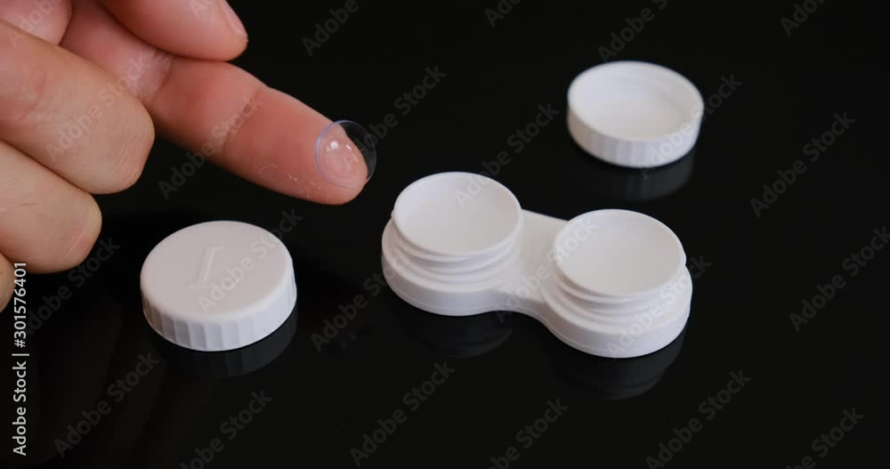 Placing a contact lens from a fingertip in a contact lens storage case filled with cleaning solution- close up detail. Placing a contact lens from a fingertip in a contact lens storage case filled with cleaning solution- close up detail.