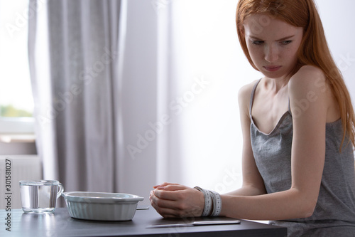 Young girl with eating disorder sitting with her hands tied with measuring tape