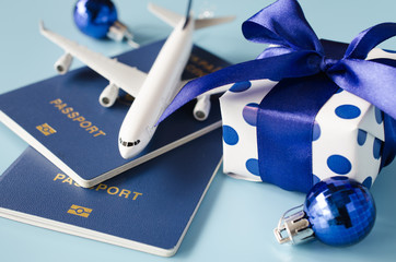 Christmas or New Year travel concept. Toy airplane with passports and gift box on blue background.