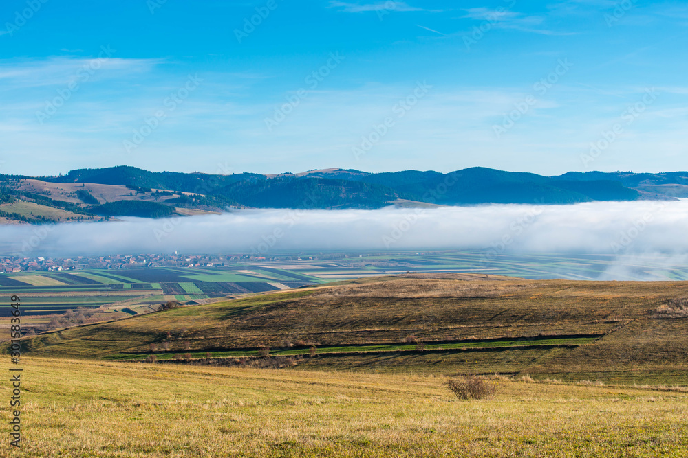 Forming fog over small village in the valley ,view from the top of the hill, blue sky with white clouds at autumn.