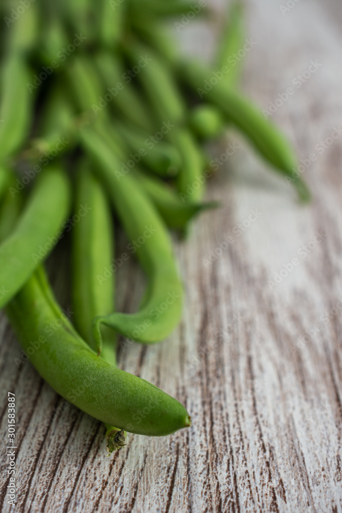 Top view of green beans, the first focused, the rest out of focus, on light wooden background, in vertical Top view of green beans, the first focused, the rest out of focus, on light wooden background, in vertical